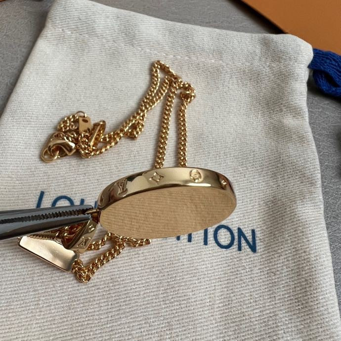 Gold-tone round logo pendant necklace with chain resting on a fabric pouch