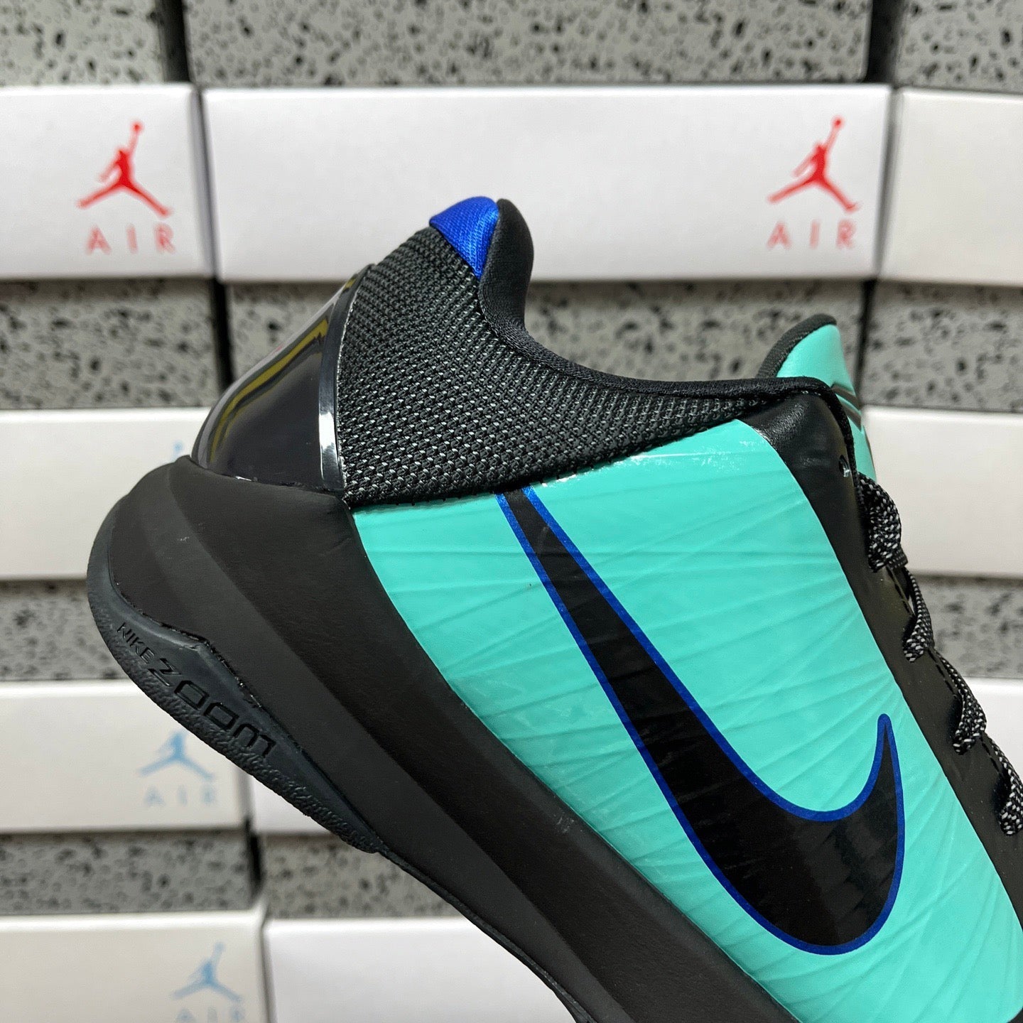 Black and teal basketball shoe with textured side and blue swoosh on teal stripe.