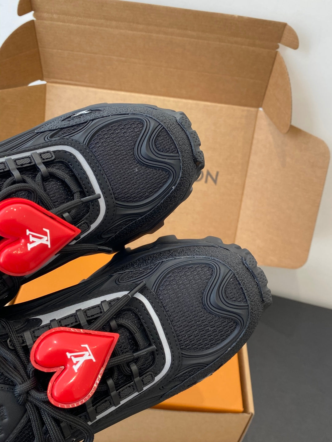 Black sneakers side panel with red LV heart lace charm and textured overlays