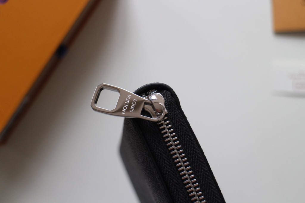Small Louis Vuitton zip wallet zipper pull with metal tab and stitched black fabric.
