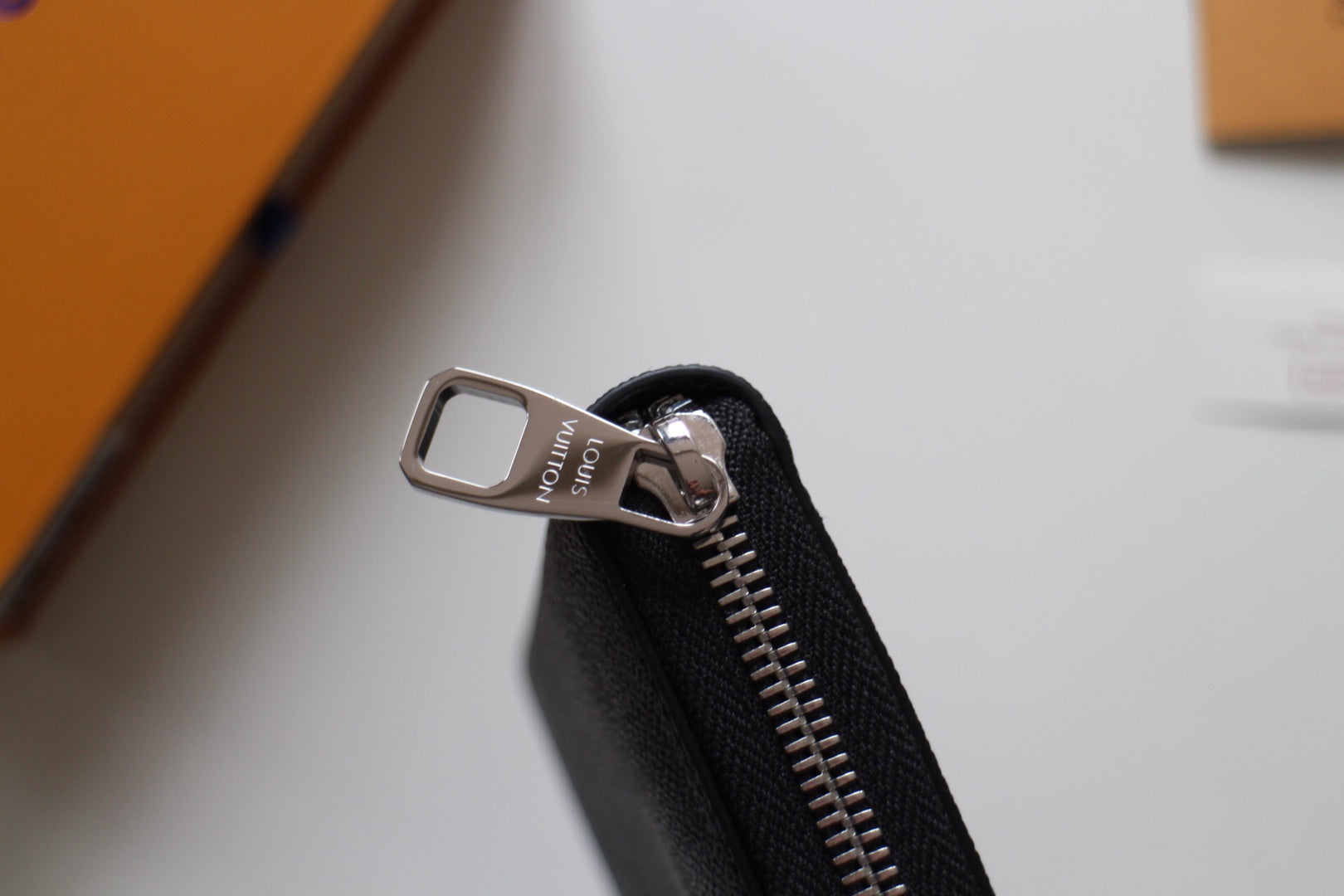 Small Louis Vuitton zip wallet zipper pull with metal tab and stitched black fabric.