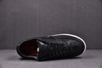 Black low-top sneaker with black laces, embossed upper pattern, white midsole
