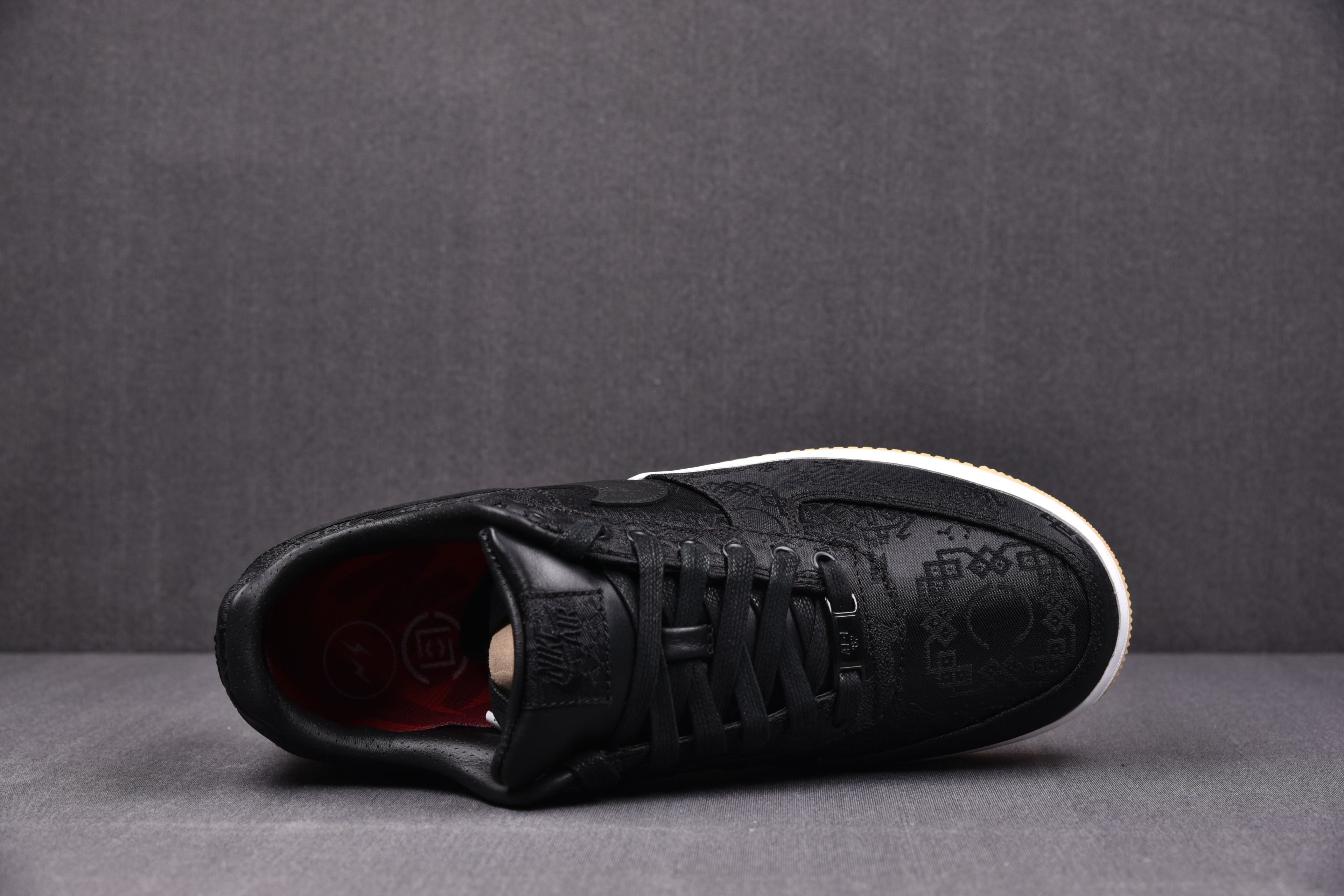 Black low-top sneaker with black laces, embossed upper pattern, white midsole