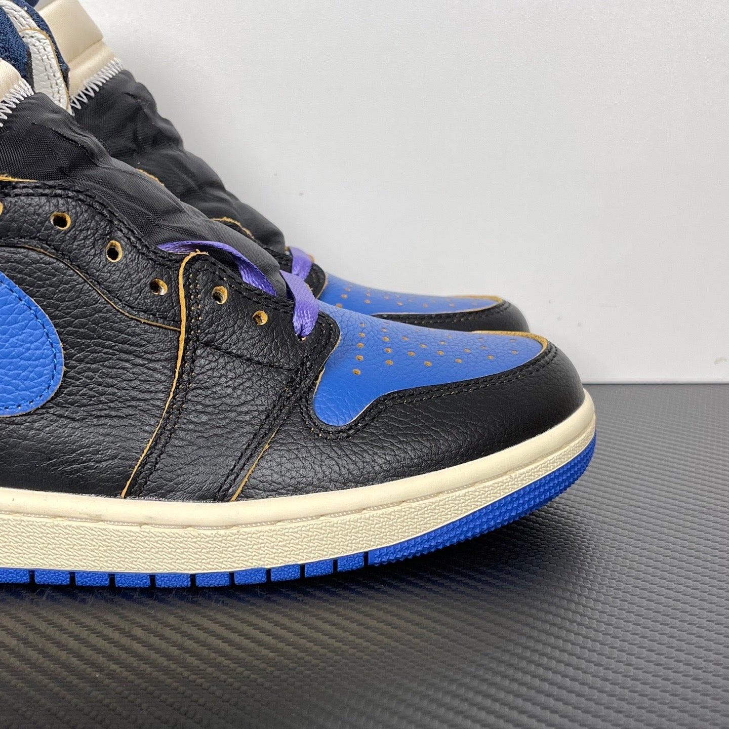 High-top sneakers side view with black leather, bright blue panels, cream midsole, purple laces