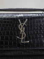 YSL croc-embossed flap close-up with YSL monogram hardware on black bag.