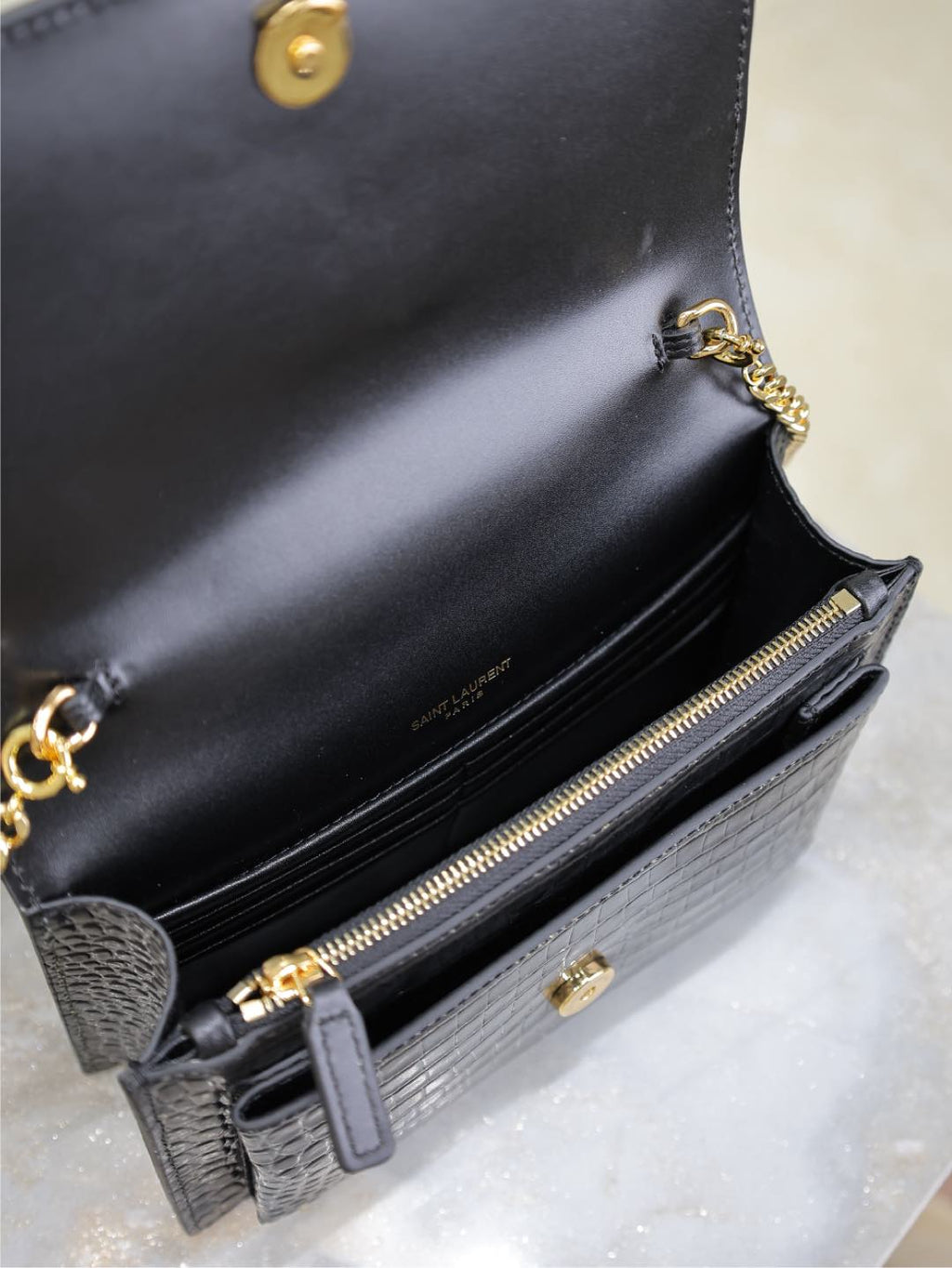 Black leather wallet bag open view with gold-tone zip, button, and chain strap.