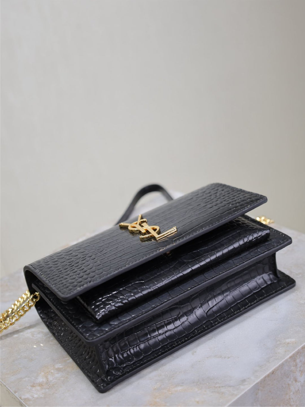 Black croc-textured flap bag with gold-tone YSL logo and chain strap.
