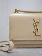 YSL cream bag close-up with gold-tone YSL logo on front flap and top handle loops