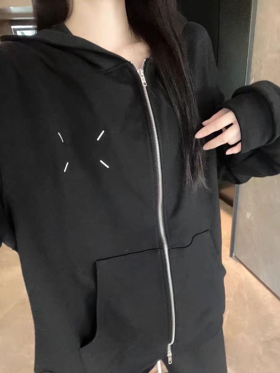 Black zip-up hoodie with hood and front zipper, chest graphic; model wearing