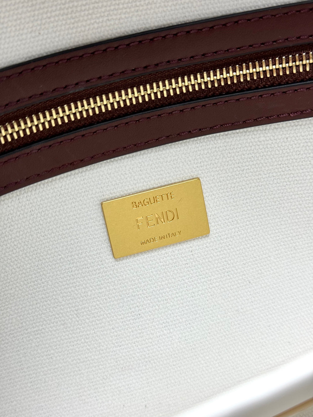 Close-up of gold 'FENDI' brand label on white fabric with maroon leather edge