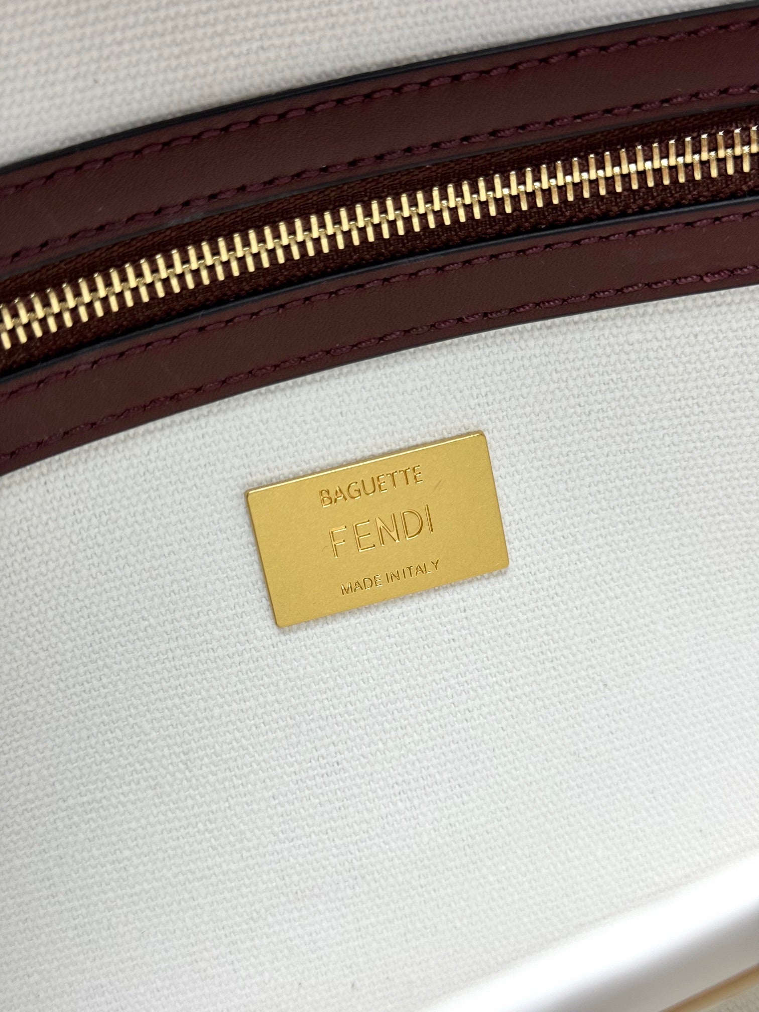 Close-up of gold 'FENDI' brand label on white fabric with maroon leather edge