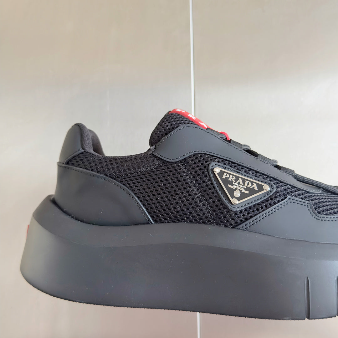 Prada unisex sneaker, close side view: dark gray mesh with overlays and red lace tab