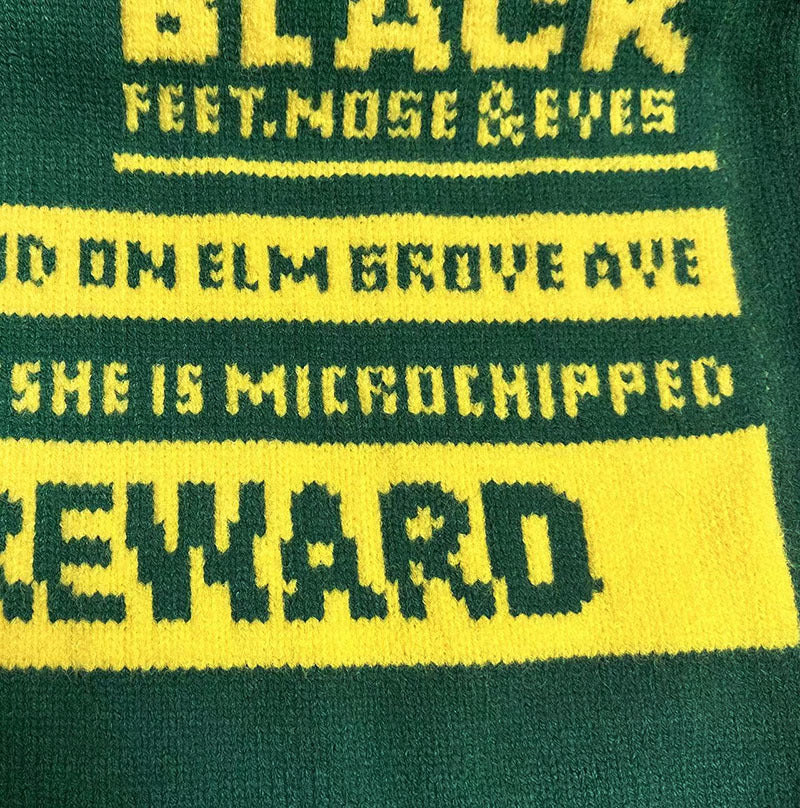 Green knit sweater closeup with yellow “BLACK” lettering and band