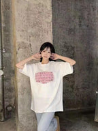 White T-shirt worn by model with pink logo graphic print on the front
