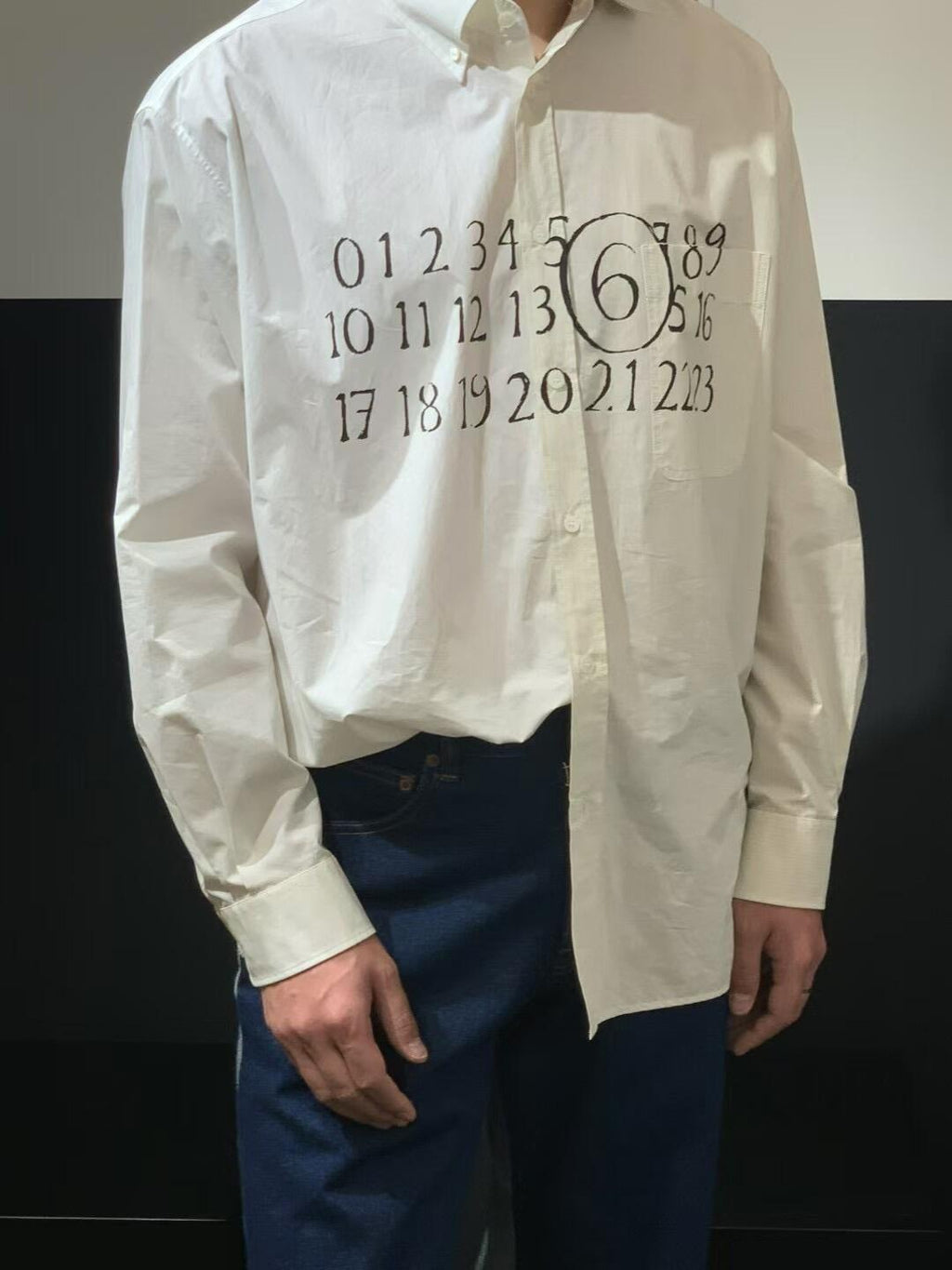 White button-up shirt with black number graphic on chest; cuffs and buttons visible