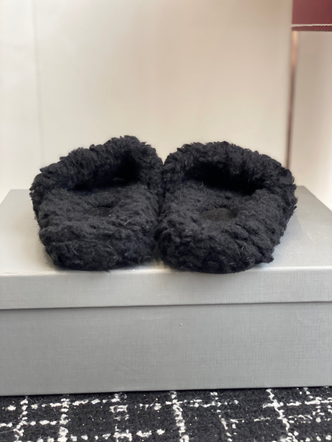 Black fuzzy slide sandals resting on a white box