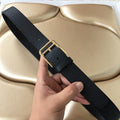 Dark textured leather belt with gold-tone rectangular buckle and keeper, held in hand