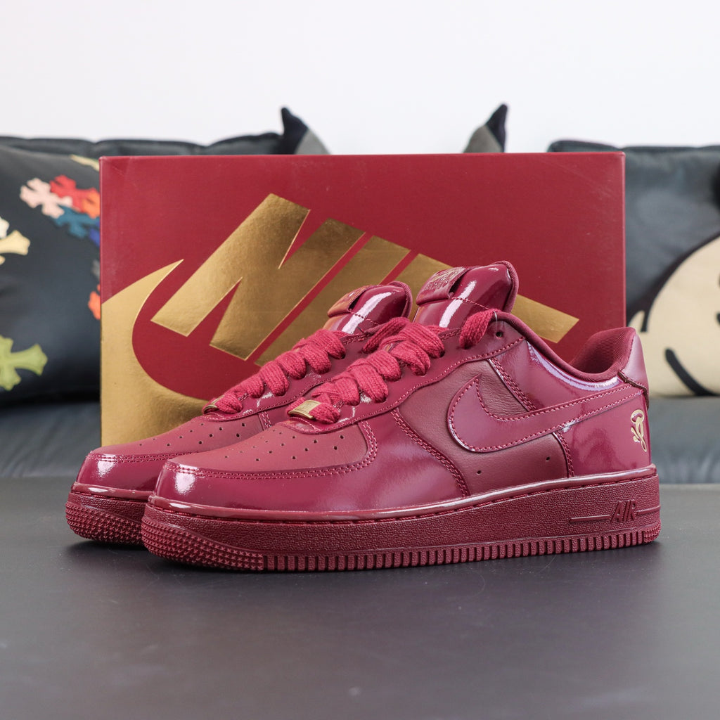 Burgundy low-top sneakers with gold swoosh accents, displayed in red shoe box
