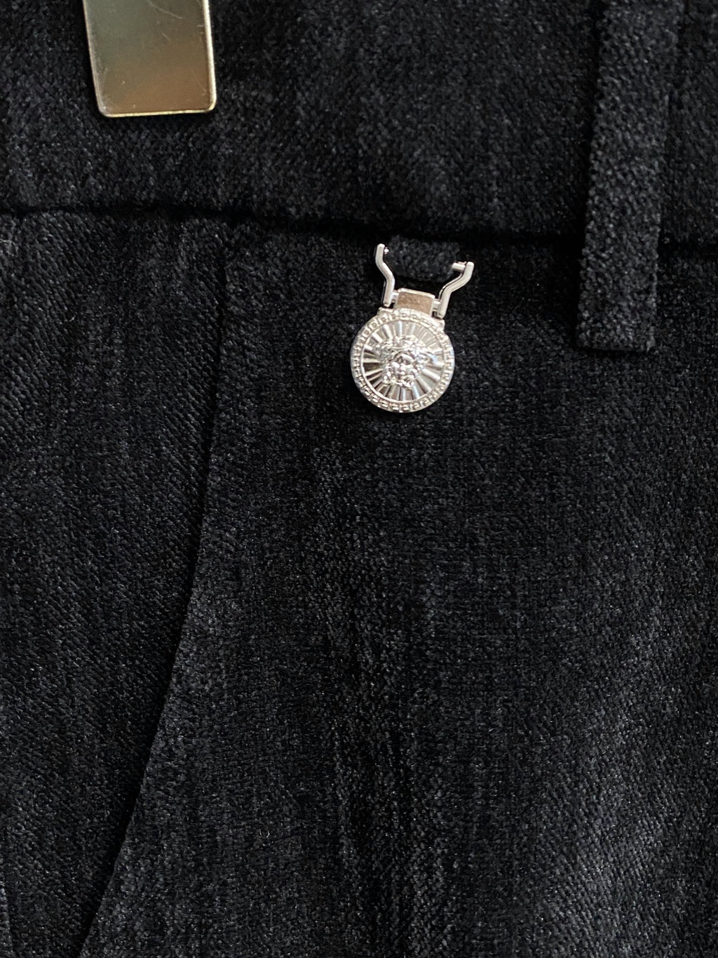 Black trousers with fabric-covered waistband button and decorative charm