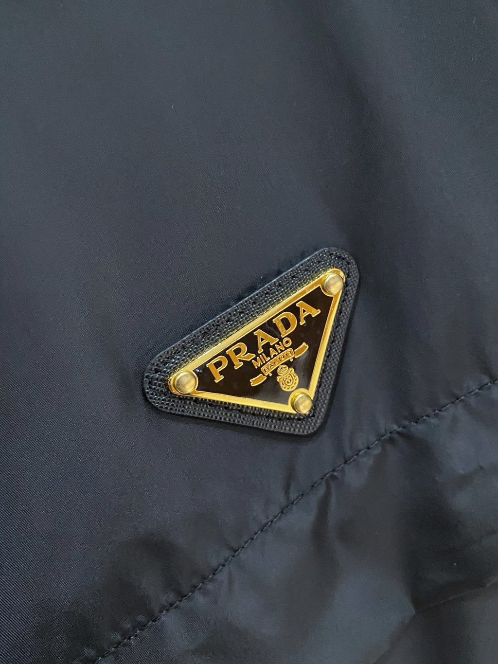Prada logo patch on black hooded jacket chest, textured fabric with gold trim.