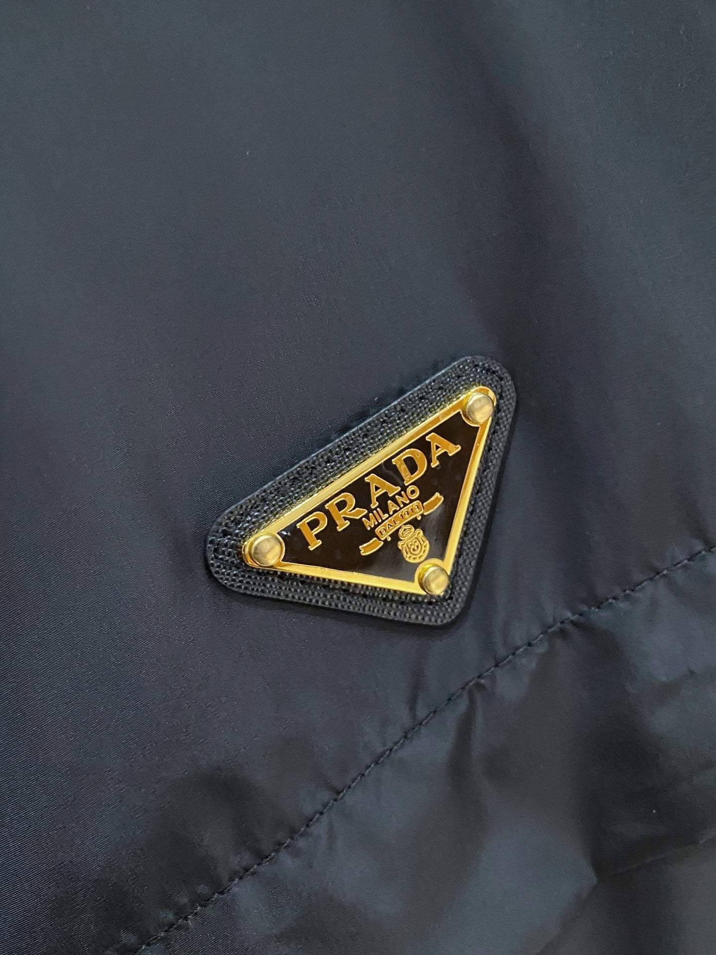 Prada logo patch on black hooded jacket chest, textured fabric with gold trim.