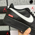 Black low-top sneaker with white swoosh, Supreme patch, and thick dark sole