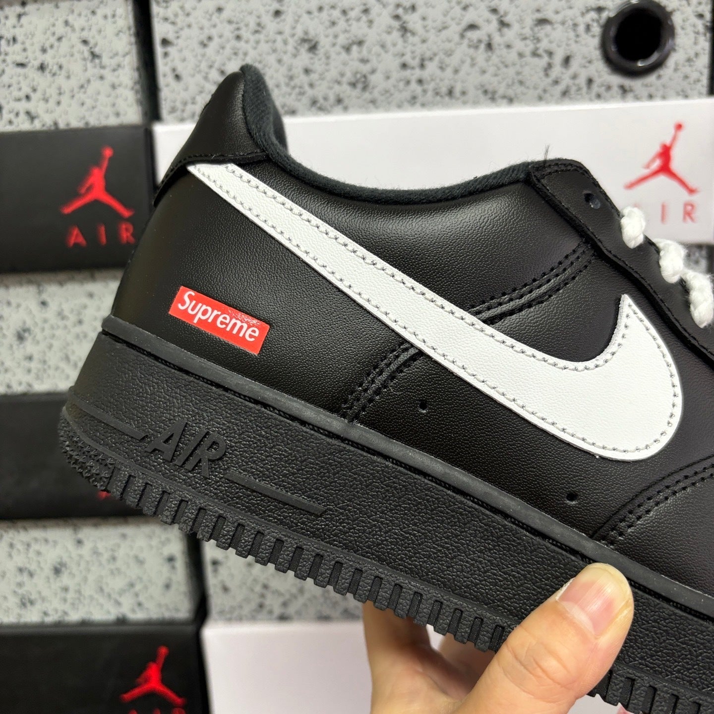 Black low-top sneaker with white swoosh, Supreme patch, and thick dark sole
