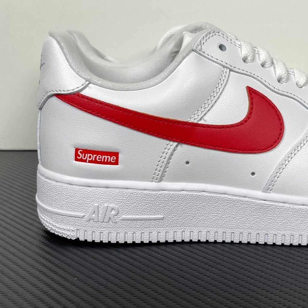 White low-top sneakers with red swoosh, Supreme patch, and AIR text on midsole.