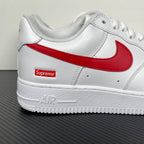 White low-top sneakers with red swoosh, Supreme patch, and AIR text on midsole.