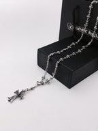 Silver-tone chain necklace with cross charms, laid on a black gift box