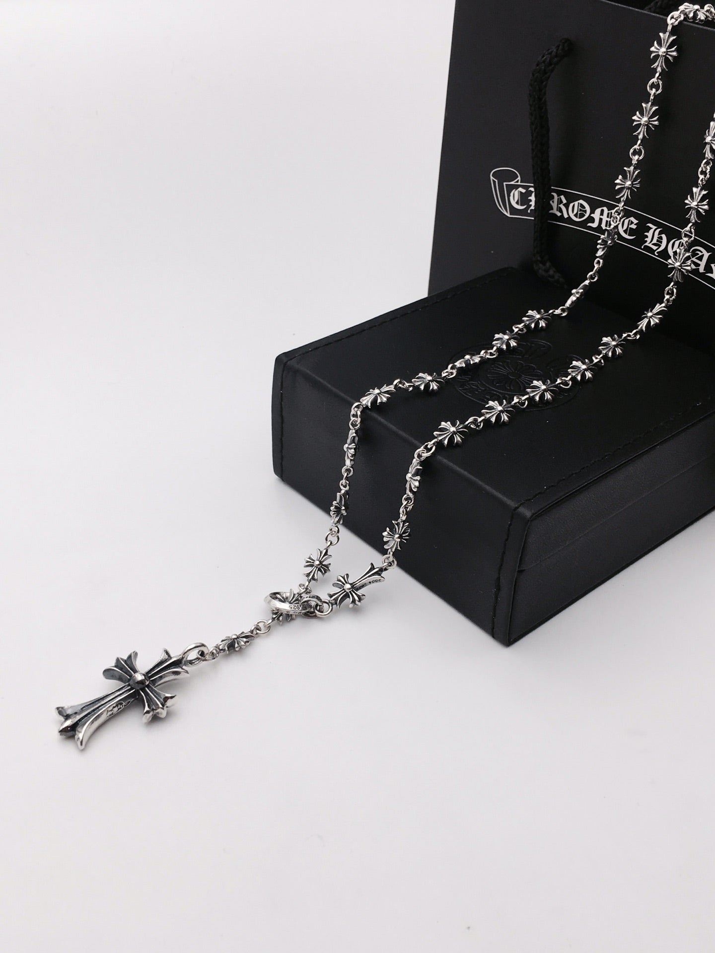 Silver-tone chain necklace with cross charms, laid on a black gift box