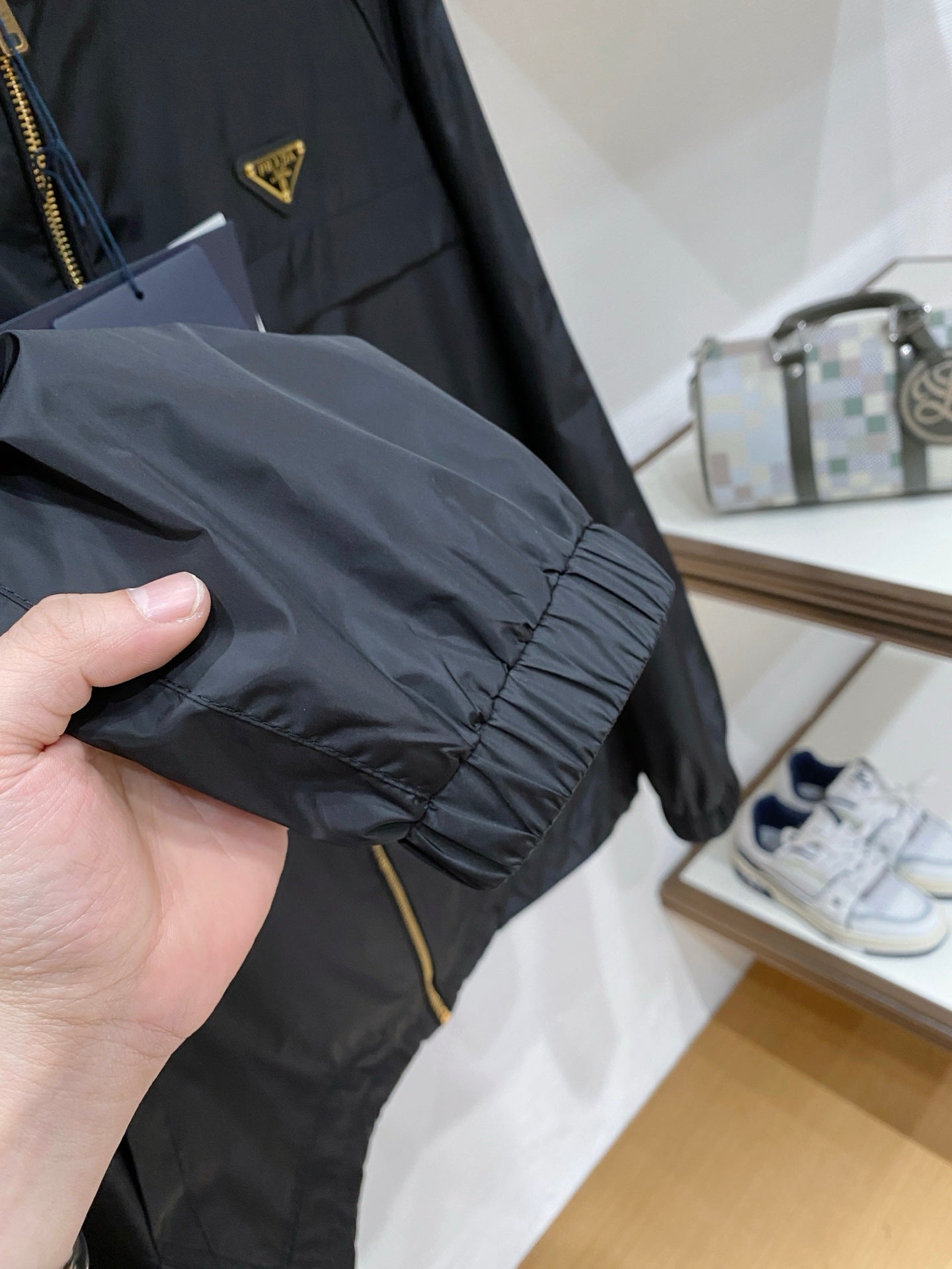 Black hooded jacket fabric and sleeve cuff, hand holding near gold zipper.