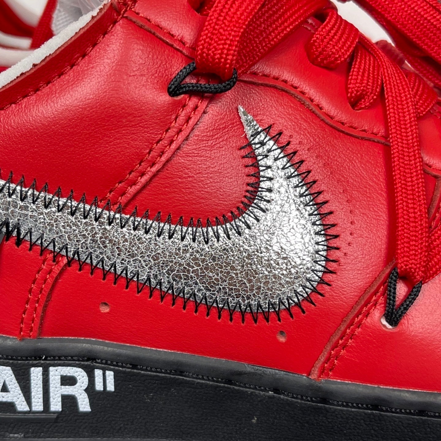 Red leather sneakers close-up, silver swoosh with zigzag stitching, black outsole