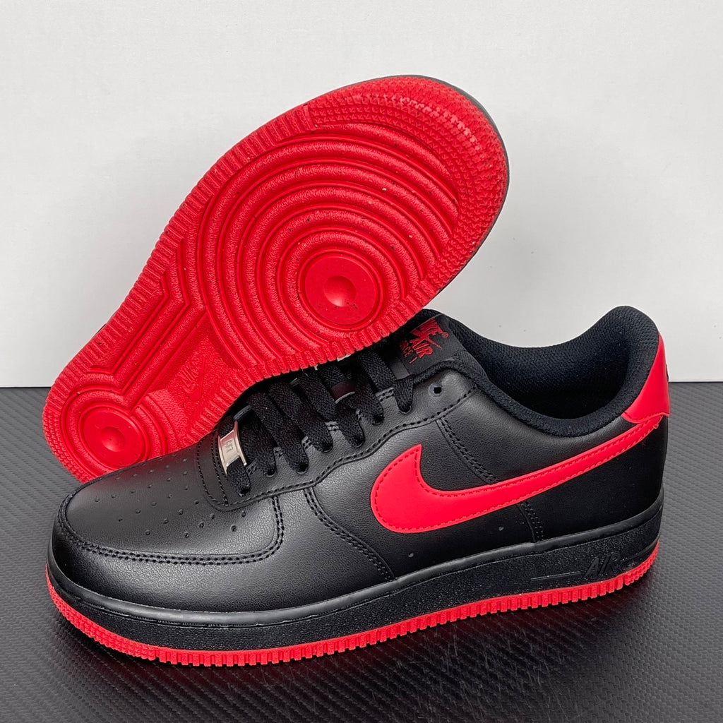 Black low-top sneakers showing red traction outsole with tread detail