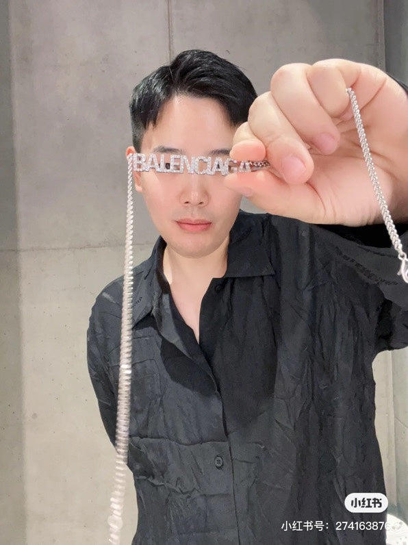 Silver Balenciaga logo pendant necklace held in hand by chain