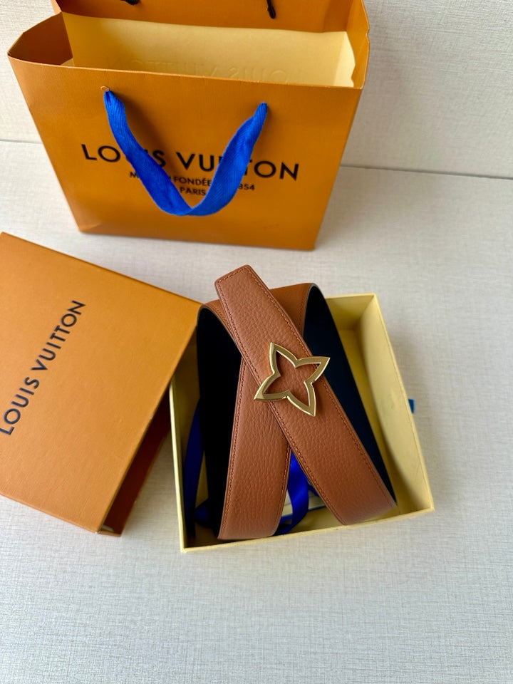 Tan belt with dark navy star buckle inside open packaging, angled view
