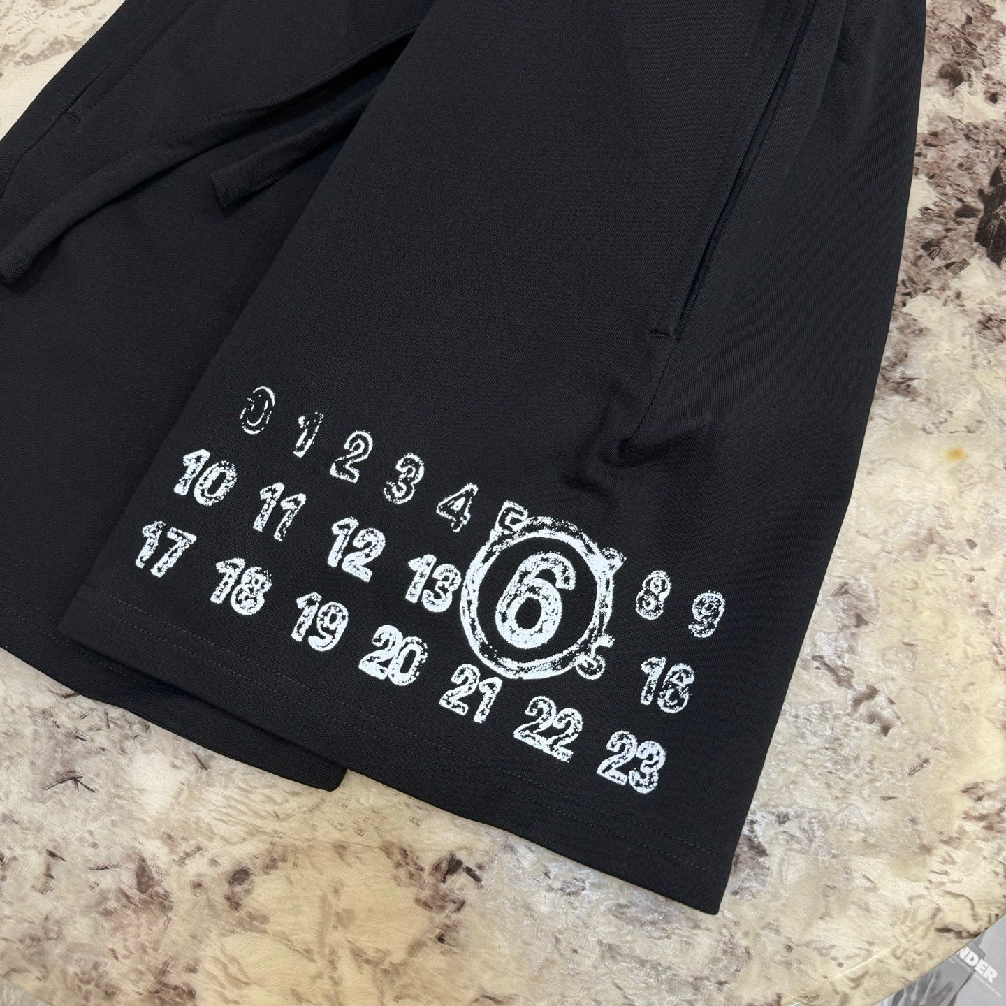 Black drawstring shorts close-up: large '6' and number print on hem