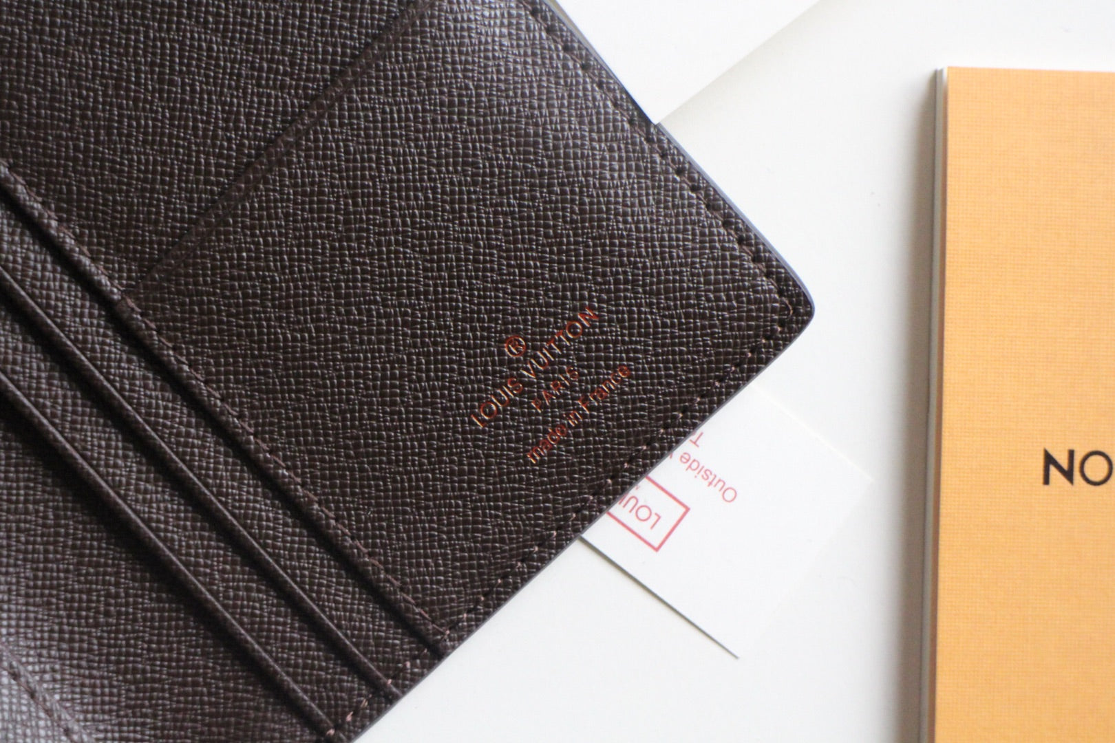 Louis Vuitton small wallet front panel with embossed logo and dark textured leather