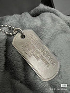 Silver-tone dog tag pendant on beaded chain over gray faux-fur fabric