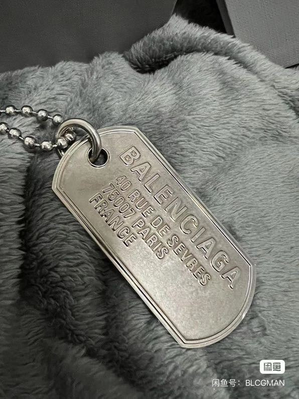 Silver-tone dog tag pendant on beaded chain over gray faux-fur fabric