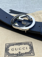 Navy leather belt with large silver-tone circular buckle, embossed logo center