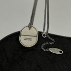 Silver-tone chain necklace with round logo pendant and oval tag charm