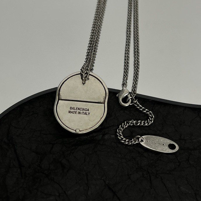 Silver-tone chain necklace with round logo pendant and oval tag charm