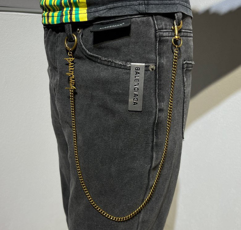 Balenciaga gold logo chain accessory on dark jeans with brand label tag