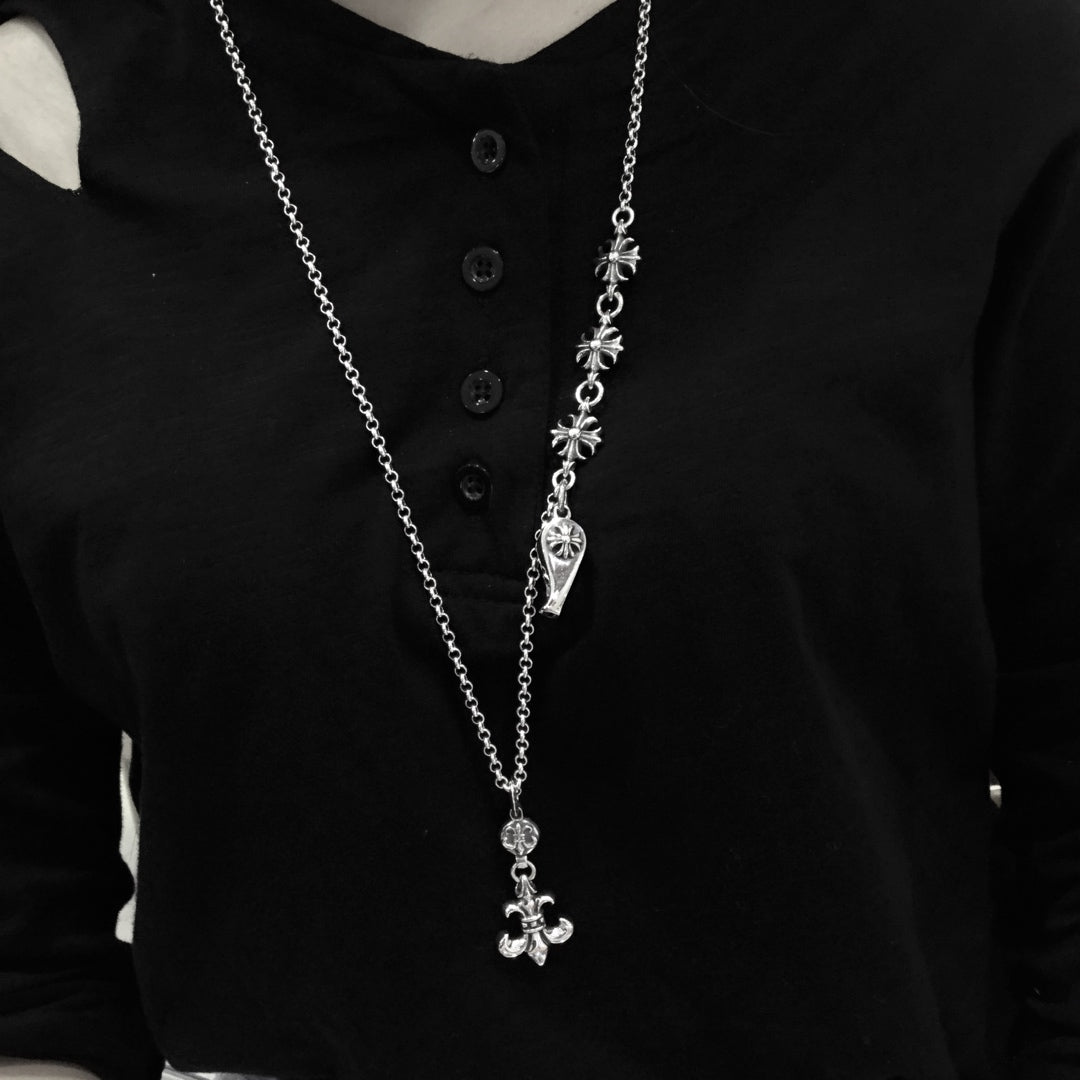 Silver chain necklace with dagger-like and cross charms over a black shirt