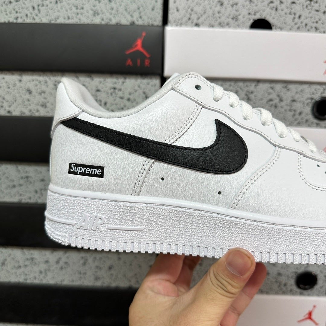 White low-top sneakers with black swoosh and Supreme label on side, close-up