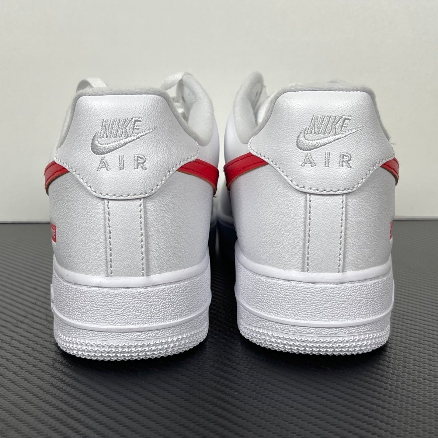 White low-top sneakers with red heel stripe and Nike AIR text on back, lace-up.