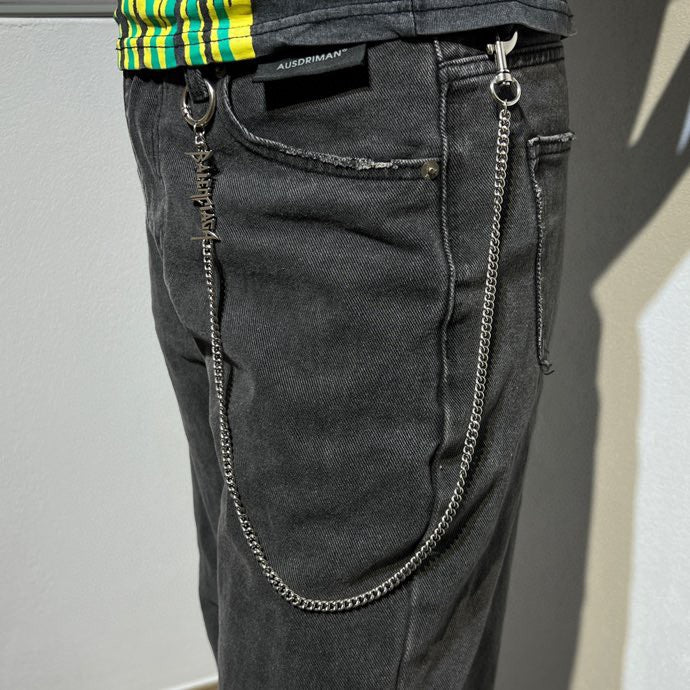 Silver-tone chain keychain with logo charm on dark jeans pocket