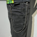 Silver-tone chain keychain with logo charm on dark jeans pocket