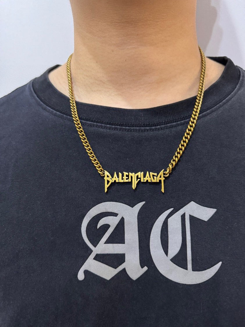 Balenciaga logo charm necklace on dark crewneck shirt, twisted gold chain